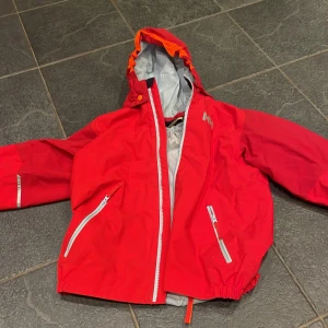 Jacka Helly Hansen - Säljer en röd vindjacka från Helly Hansen med huva och dragkedja. Jackan har vita detaljer och elastiska muddar. 💕