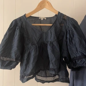 Mörkblå blus  - Säljer en mörkblå blus med v-ringning och trekvartsärmar. Blusen har spetsdetaljer och en luftig passform, perfekt för en stilren look som knappt är andvänd💙