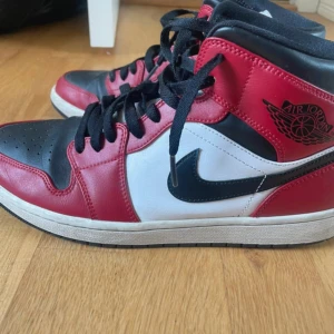 Nike Air Jordans i rött, svart och vitt - Snygga Nike Air Jordans i klassisk färgkombination av rött, svart och vitt. Skorna har en hög modell med snörning och den ikoniska Air Jordan-loggan på sidan. Perfekta för dig som vill ha en stilren och sportig look.