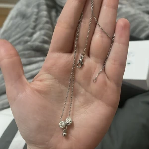 Silverhalsband med blomma och pärla - Elegant silverhalsband med en fin blomma och en liten pärla som hänge. Perfekt för att ge en subtil glans till din outfit. Kedjan är tunn och smidig med ett enkelt lås.