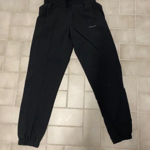 Svarta mjukisbyxor - Snygga svarta joggers med elastisk midja och muddar vid bensluten. Perfekta för en avslappnad springtur. Diskret logga på ena benet.