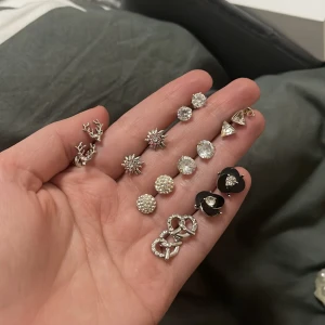 Set med olika örhängen i silver och svart - Ett set med flera par örhängen i olika stilar. Inkluderar silverfärgade stjärnor, glittriga stenar, svarta hjärtan och trianglar. Perfekt för att mixa och matcha till olika tillfällen.“Varje sort kostar 40 kr.” Men alla koster  280 