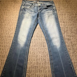 Blå jeans med broderade bakfickor - Snygga blå jeans från Anya Jeans med unika broderade detaljer på bakfickorna. De är bootcut. Midja rakt över: 40cm. Lår: 28cm. Innerben: 81cm