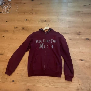 Vinröd hoodie med tryck (Aim for the Moon) - Snygg vinröd hoodie med dragkedja och tryck på framsidan. Perfekt för en avslappnad stil. Den har långa ärmar och en bekväm passform. Priset kan diskuteras.