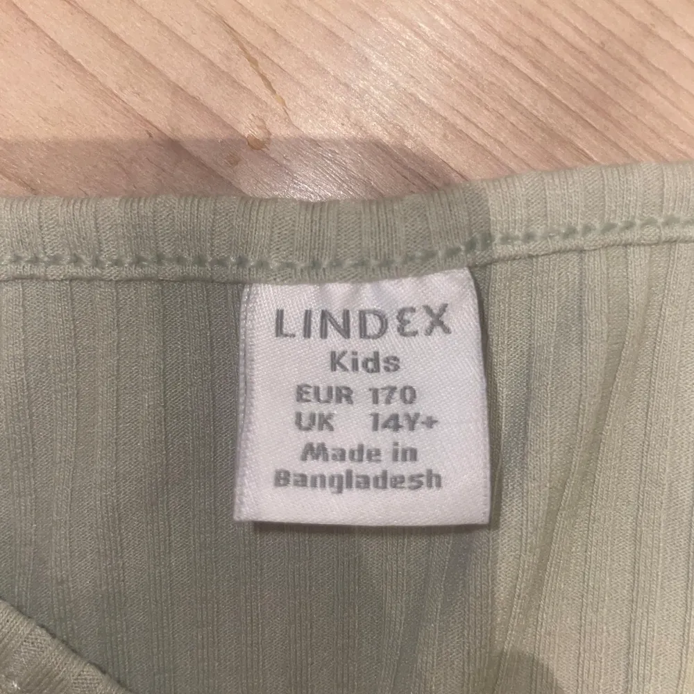 Snygg grön ribbad topp från Lindex med v-ringning och knytning framtill. Perfekt för en avslappnad stil. Kortärmad design som passar bra till både jeans och kjol.. Yläosat.