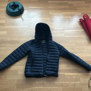 Mörkblå pufferjacka från Save the Duck - Säljer en svart pufferjacka från Save the Duck i storlek M. Jackan är ultralätt och har en huva samt dragkedja framtill. Den är tillverkad med Plumtech-teknologi och är 100% djurfri. Perfekt för kyliga dagar! Nypris ligger runt 1400kr