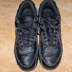 Svarta Nike Air Max sneakers - Säljer ett par svarta Nike Air Max sneakers med klassisk design och snörning. Skorna har en robust sula och är perfekta för en sportig look.