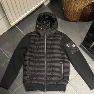 Svart cardigan från Moncler - Snygg svart cardigan från Moncler med huva och dragkedja. Jackan har långa ärmar och en quiltad design på framsidan. Perfekt för kyligare dagar.