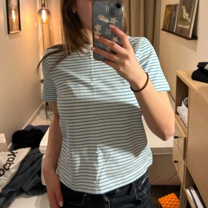 Cos tshirt - Vit T-shirt med blå ränder från Cos. Sparsamt använd och i mycket bra skick. Materialet är rejält och lite tjockare än en ”vanlig” T-shirt. Strl S