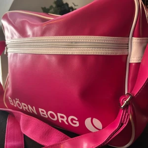 Stor rosa crossover bag från Björn Borg! - Stor ceriserosa crossover bag med ett stort fack och flera mindre både invändigt och på framsidan samt rejäl justerbar axelrem. Mått: 35 x 30 cm. Väskan är i mycket fint skick!