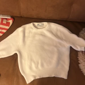 Vit tröja från Zara - Säljer en stilren vit tröja från Zara. Den är mjuk och har en rund halsringning med ribbade kanter. Perfekt för en enkel och snygg look.