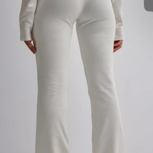Vita ribbade byxor - Snygga vita ribbade byxor med bootcut-stil. Perfekta för en stilren look, dessa byxor har en tight passform upptill och vidgar sig vid anklarna. Tillverkade i ett mjukt och bekvämt material. Helt ny med prislappen på