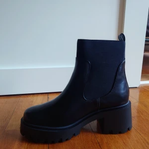 Svarta Chelsea boots strl 39 - Svarta Chelsea boots i läderimitation med semihög klack och rund tå. Storlek 39. Helt oanvända med etiketter och originalförpackning kvar. Nypris 429.