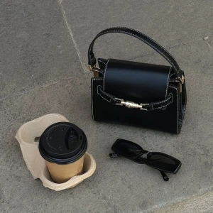 Svart axelväska med gulddetaljer - Snygg svart axelväska i skinn med eleganta gulddetaljer. Perfekt för både vardag och fest. Väskan har en stilren design med en praktisk axelrem och ett dekorativt spänne framtill. Axelremmen är justerbar och kan även tas bort. Endast använd en gång så är inprincip som ny. 