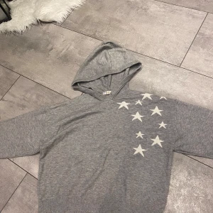 Grå hoodie med stjärnor från Gina Tricot - Säljer en supermysig grå hoodie från Gina Tricot med vita stjärnor på framsidan och en stor stjärna på baksidan. Perfekt för en chill dag eller när du vill vara bekväm men ändå snygg. Den har en klassisk passform och är gjord i mjukt material. Hör av dig om du är intresserad! ⭐