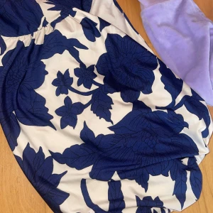 Blommig oneshoulder klänning - Snygg oneshoulder topp med ett iögonfallande blommigt mönster i marinblått och vitt. Perfekt för sommarens fester eller en stilfull dag på stan. Toppen har en unik design med en axel och är tillverkad i ett bekvämt material. Den är från hm och i ny skick