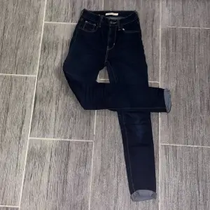 Säljer ett par snygga Levi's 721 High Rise Skinny jeans i mörkblå färg. De är högmidjade och har en tight passform som framhäver figuren. 