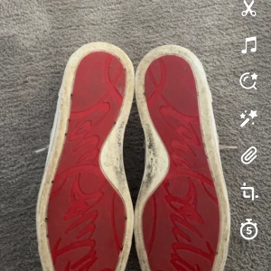 Vita sneakers med nitar - Säljer ett par vita sneakers med coola nitar på tån och klassisk röd sula. De har snörning och är i bra skick. Perfekta för att ge din outfit en edgy touch!