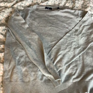 Grå tröja från GANT - Säljer en grå tröja från GANT i storlek M. Tröjan är i bomull och har en klassisk rund halsringning. Perfekt för både vardag och lite finare tillfällen. Den har långa ärmar och en liten broderad logga på bröstet. Superbekväm och lätt att matcha med det mesta! Pris kan diskuteras.