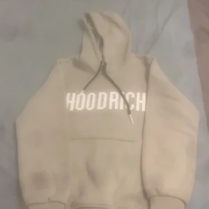 Beige hoodie från Hoodrich - Säljer en snygg beige hoodie från Hoodrich. Den är i storlek M och har en stor ficka på magen. Hoodien har en justerbar huva med svarta snören och texten 'HOODRICH' tryckt i vitt på bröstet. Perfekt för höst och vinter, supermysig och stilren!