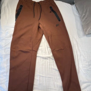 Nike Tech Byxor - Säljer ett par bruna Nike Tech byxor i storlek M. Byxorna är helt oanvända och därför i nyskick! kostar nästan 1000kr nya 🤩och säljer för endast 259. Priser kan diskuteras vid snabb affär och Hör av dig vid frågor eller likande!