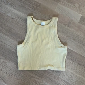 Gul ribbad croppad linnetopp - Säljer en superfin gul ribbad croppad linnetopp. Perfekt för sommaren och kan stylas med både jeans och kjol. Toppen är ärmlös och har en tight passform. Den är i bra skick och redo för en ny ägare!