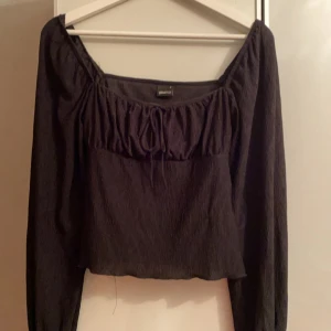 Svart topp från Gina Tricot - Säljer en snygg svart topp från Gina Tricot. Den har långa ärmar och en söt knytning framtill. Perfekt för både vardag och fest!😊