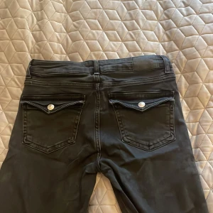 Svarta bootcut jeans - Säljer ett par svarta bootcut jeans från lager 157 i storlek S. De har en klassisk femficksdesign med silverfärgade knappar och nitar. Jeansen är i bra skick och har en snygg passform som är tight upptill och utsvängda nedtill. Perfekta för både vardag och fest! Låg midja