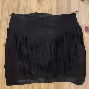 Svart kjol från JF Lefon - Säljer en snygg svart kjol från JF Lefon i storlek 38 (M). Kjolen har en cool design med fransar som ger den en unik look. Perfekt för en fest eller en utekväll! 🖤