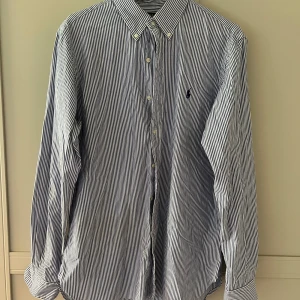 Ralph Lauren Skjorta  - Jättesnygg blåvit randig skjorta från Polo Ralph Lauren. Skjortan är i jättebra skick och knappt använd. En jätteskön och snygg skjorta som passar till det mesta! Passar runt storlek M och L. 