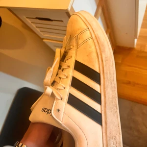  Adidas skor - Säljer ett par vita Adidas sneakers med svarta ränder. Skorna är i välanvänt skick med synliga tecken på användning, särskilt på sulorna. De har snörning och är gjorda av skinn. Perfekta för vardagsbruk! Kända rapparen drottz använt dessa på konsär 