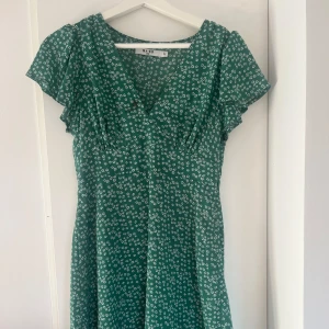 Grön blommig klänning från NA-KD - Säljer en kort grön blomstermönstrad klänning ifrån NA-KD. Använd två gånger i storlek xs.