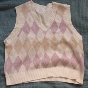 Beige och rosa stickad väst med diamantmönster - Säljer en superfin stickad väst i beige och rosa med ett snyggt diamantmönster från Lindex. Perfekt för höst och vår, den är i nyskick. Skriv gärna till mig om du har frågor!