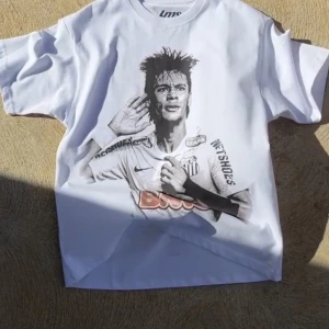 Vit t-shirt med fotbollstryck - Säljer en vit t-shirt från Lupo med ett coolt fotbollstryck på både fram- och baksidan. T-shirten har korta ärmar och är i nyskick. Perfekt för fotbollsfans som vill visa sitt stöd! 🏆