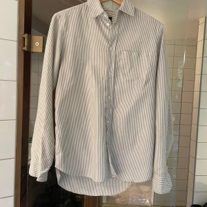 Randig skjorta från A.P.C. - Säljer en stilren och klassisk randig skjorta från A.P.C. i storlek S. Skjortan är vit med tunna svarta ränder och har långa ärmar. En mindre defekt vid en av knapparna, kan skicka bilder vid intresse men inget som märks när man bär den