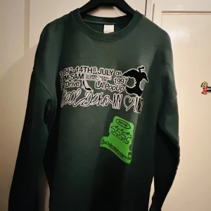 Mörkgrön sweatshirt från Zara - Säljer en cool mörkgrön sweatshirt från Zara med tryck både fram och bak. På framsidan finns text och grafik i vitt och grönt, och baksidan har ett stort tryck med gröna detaljer. Perfekt för en avslappnad stil!