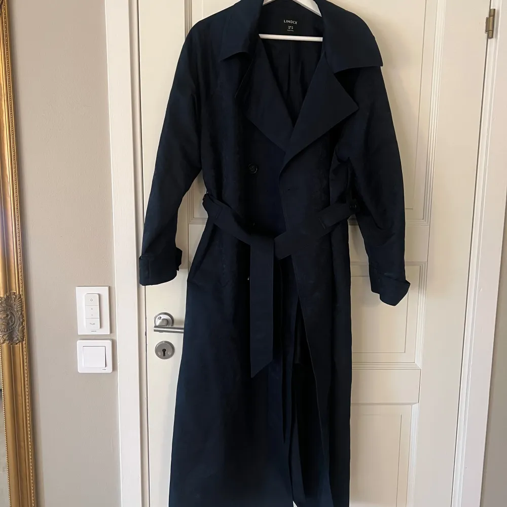 Oanvänd trenchcoat. Marinblå, vattenavvisande. Köpt för 1499kr.. Jackor.