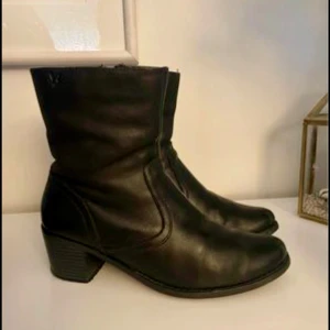 Svarta boots från Caprice - Säljer ett par snygga svarta boots från Caprice i skinn. De har en låg klack och är perfekta för både vardag och fest. Skorna är i bra skick och har en bekväm passform. Jag har storlek 40 och de passar mig perfekt. De står dock storlek 39 i skon. 