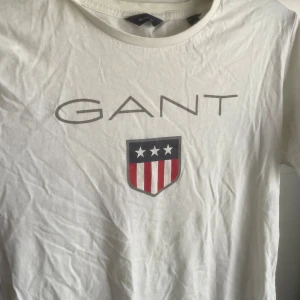 Gant vit T-shirt storlek 158/164 cm 13-14 years  - Vit T-shirt med GANT-logotypen på framsidan. T-shirten har en rund halsringning och korta ärmar.