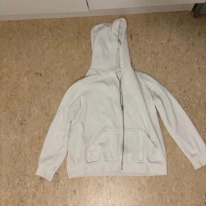 Vit hoodie med dragkedja - Säljer en vit hoodie i nyskick. Den har en dragkedja framtill och en stor ficka på magen. Perfekt för kyliga dagar eller mysiga hemmakvällar. Passar till det mesta och är superbekväm!