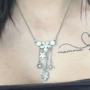 Silverfärgat halsband med blommor och stjärnor - Säljer ett superfint silverfärgat halsband med flera hängande detaljer. Halsbandet har små blommor och stjärnor som dinglar från kedjan. Men tyvärr kommer det inte till andvändning 💕💕