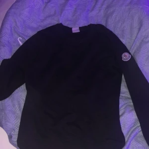 Svart tröja med märke på ärmen - Säljer en stilren svart tröja med ett coolt märke på ärmen. Perfekt för både vardag och fest. Tröjan har långa ärmar och är i ett mjukt material som känns skönt mot huden. Passar perfekt till jeans eller kjol!