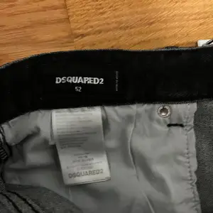 Säljer ett par snygga svarta jeans från Dsquared2 i storlek 52. De har en cool, sliten look med färgstänk och slitningar på framsidan. Perfekta för en avslappnad men stilren outfit. Jeansen har en klassisk femficksdesign och knappgylf.