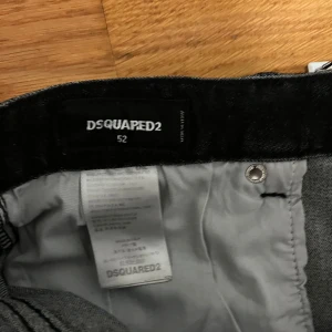 Svarta jeans från Dsquared2 - Säljer ett par snygga svarta jeans från Dsquared2 i storlek 52. De har en cool, sliten look med färgstänk och slitningar på framsidan. Perfekta för en avslappnad men stilren outfit. Jeansen har en klassisk femficksdesign och knappgylf.