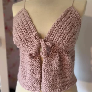 Rosa virkad topp med knyt - Säljer en superfin rosa virkad topp med knyt framtill. Den är ärmlös och perfekt för sommardagar. Toppen har en söt och unik design som verkligen sticker ut. Passar perfekt till både jeans och kjol!