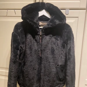 Svart pälsjacka från Pull&Bear - Mysig svart pälsjacka från Pull&Bear i mycket bra skick. Jackan har en dragkedja framtill och en stor huva för extra värme. 