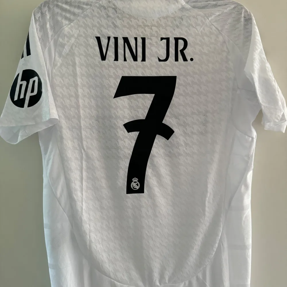 Säljer en vit Real Madrid fotbollströja från Adidas i storlek L. Tröjan är i nytt skick med korta ärmar och har klubbens emblem på bröstet. Den är tillverkad i ett lätt och andningsbart material med 'HEAT.RDY' teknologi för optimal komfort. Perfekt för alla Real Madrid-fans! Storlek L. T-shirts.