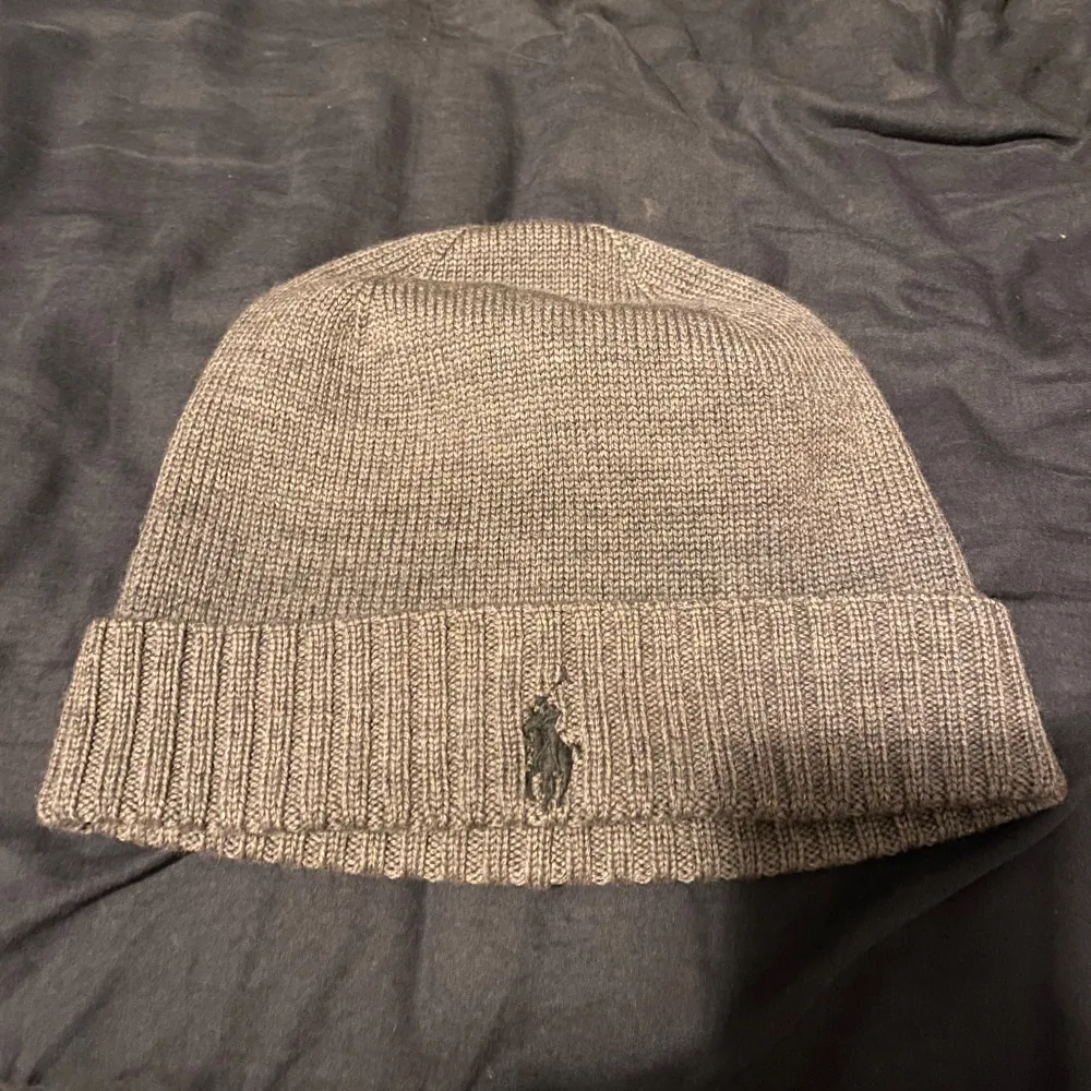 Säljer en snygg grå stickad mössa från Ralph Lauren. Den har en ribbad kant och är broderad med den klassiska loggan framtill. Perfekt för kyliga dagar och ger en stilren look. Passar både till vardags och lite finare tillfällen.. Accessoarer.