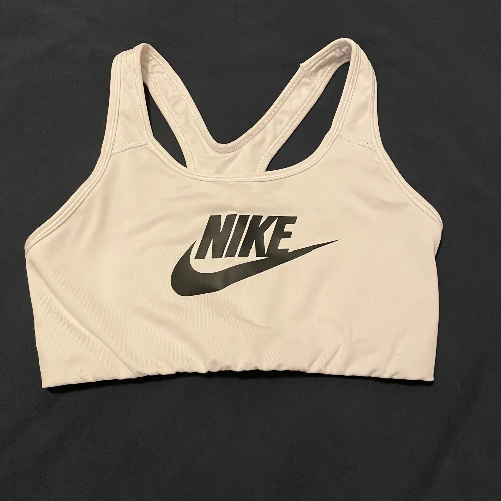 Säljer en vit sport-bh från Nike i mycket bra skick. Den har en klassisk design med Nike-loggan i svart framtill. Perfekt för träning med sin bekväma passform och stödjande material.. Sportswear.