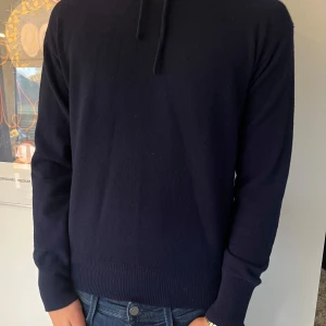 Marinblå kashmirhoodie - Säljer en stilren stickad hoodie i 100% kashmir.  Använd endast ett fåtal gånger så i mycket bra skick. Den har en klassisk design med långa ärmar och en bekväm huva. Perfekt för både höst och vinter, passar till de flesta outfits. Nypris 1299 kr. Storlek S. Normal storlek. Ser att bilderna är tagna för nära så inte hela tröjan syns i annonsen så kommer uppdatera med nya bilder så snart som möjligt. 